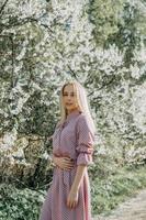 rubia niña en un primavera caminar en el jardín con Cereza flores hembra retrato, de cerca. un niña en un rosado polca punto vestido. foto