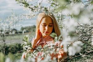 rubia niña en un primavera caminar en el jardín con Cereza flores hembra retrato, de cerca. un niña en un rosado polca punto vestido. foto