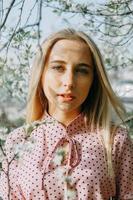 Blonde girl on a spring walk in the garden with cherry blossoms. Female portrait, close-up. A girl in a pink polka dot dress. photo