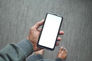 POV of young man hand holding a smart phone with white screen at home photo