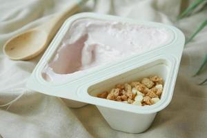 yogur fresco en un recipiente de plástico y una cuchara en la mesa foto