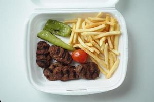 Kabab meat with potato fries in a take away packet on table photo