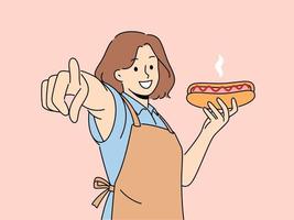 Smiling woman in apron holding hot dog point at screen. Happy waitress with fastfood in hands show at camera with finger. Vector illustration.