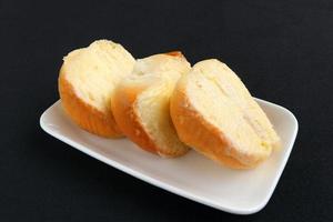 A row of fresh butter with sugar bread in half round shape on white plate and black background. Beside view. photo