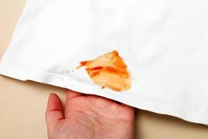 womans hand hold white shirt clothes with ketchup stain on a beige background photo