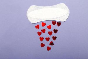almohadilla de higiene diaria para mujeres sobre un fondo morado con corazones rojos foto