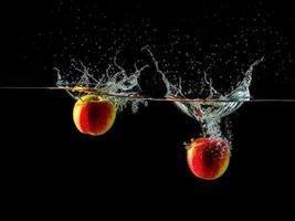 Two apples are splashing in the water and one is red. photo