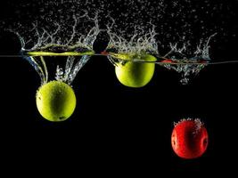 Tres manzanas son siendo caído dentro el agua tanque y el agua es salpicaduras foto