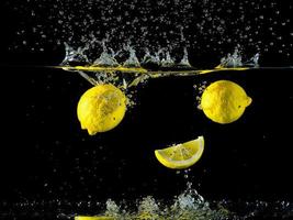 limones que cae dentro el agua creando salpicaduras con un negro antecedentes foto