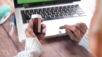 Senior woman person hand holding pill container and using laptop video