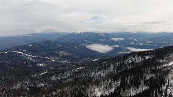 hermosa invierno montaña paisaje en un nublado día aéreo disparo. esquí recurso parte superior vista. video