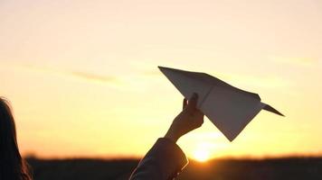 Woman launches paper airplane against sunset background. Concept of wanting to go on vacation or travel. Slow motion video