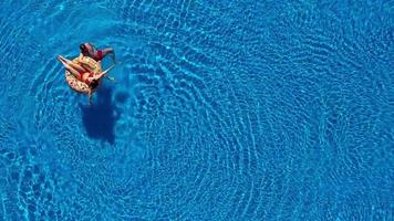 aereo Visualizza di uomo immersioni in il il piscina mentre ragazza è dire bugie su un' ciambella piscina galleggiante video