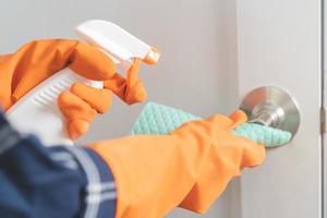 Hand of asian young woman, girl cleaning rubs dust, use rags, spray bottle on knob door of toilet room at home. Household hygiene cleanup, cleaner people, equipment or tool for cleaning. photo