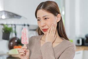 Closing eyes asian young woman touching cheek, face expression from toothache, tooth decay or sensitivity, Having  teeth problem or inflammation, suffering from health. Sensitive teeth people. photo