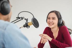Smile two asian young woman, man radio hosts in headphones, microphone while talk, conversation, recording podcast in broadcasting at studio together. Technology of making record audio concept. photo