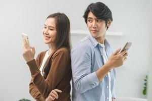 Infidelity, suspicion asian young couple love standing back to back, husband watching his wife using mobile phone, spying his girlfriend while woman typing a message, man distrust and jealousy at home photo