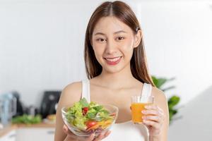 Diet, Dieting, pretty asian young woman or girl smiling, holding glass of orange juice and mix vegetables, green salad bowl. eat food is low fat good healthy. Nutritionist weight loss health person. photo