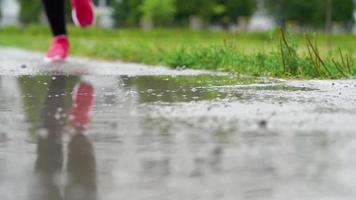 Close up of legs of a runner in sneakers. Sports woman jogging outdoors, stepping into muddy puddle. Single runner running in rain, making splash. Slow motion video