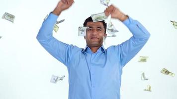 An Arab man stands on a white background, and a lot of dollar bills are suddenly thrown at him from different sides. Slow motion video