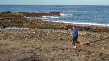 mujer carreras a lo largo el pedregoso apuntalar de el océano. sano activo estilo de vida video