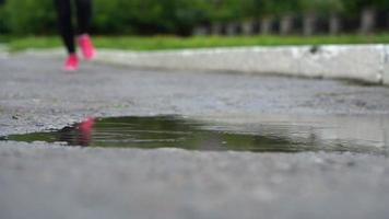 fechar acima do pernas do uma corredor dentro tênis. Esportes mulher corrida ao ar livre, pisar para dentro turvar poça. solteiro corredor corrida dentro chuva, fazer respingo video