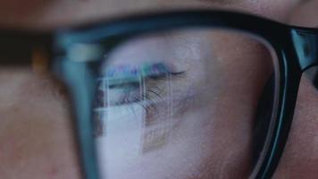 Woman in glasses looking on the monitor and surfing Internet at night. The monitor screen is reflected in the glasses video