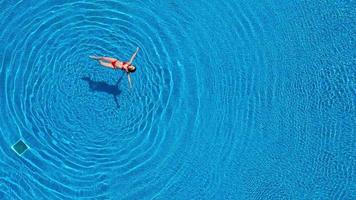 View from the top as a woman in a red swimsuit swimming and lying on her back in the pool. Relaxing concept video