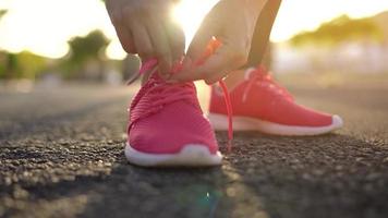 cerca arriba de mujer atadura zapato cordones y corriendo a lo largo el palma avenida a puesta de sol video