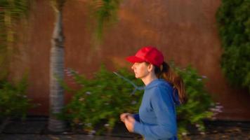 Woman tying shoelaces and starts jogging along the street among the tropical alley. Healthy active lifestyle video