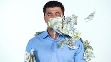 An Arab man stands on a white background, and a lot of dollar bills are suddenly thrown at him from different sides. Slow motion video