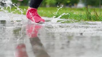 fechar acima do pernas do uma corredor dentro tênis. Esportes mulher corrida ao ar livre, pisar para dentro turvar poça. solteiro corredor corrida dentro chuva, fazer splash. lento movimento video