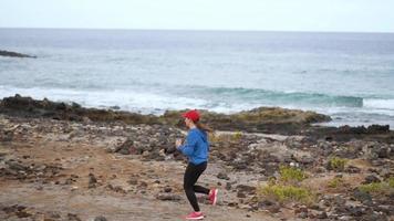 Woman runs along the stony shore of the ocean. Healthy active lifestyle. Slow motion video