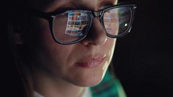 Woman in glasses looking on the monitor and surfing Internet at night. The monitor screen is reflected in the glasses video