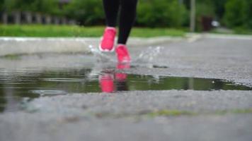 Close up of legs of a runner in sneakers. Sports woman jogging outdoors, stepping into muddy puddle. Single runner running in rain, making splash video