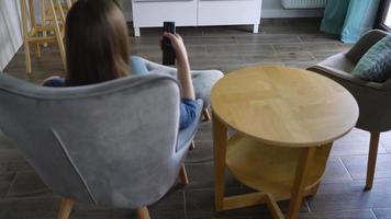 Frau ist Sitzung im ein Stuhl, Aufpassen Fernseher mit ein Grün Bildschirm, Schalten Kanäle mit ein Fernbedienung Kontrolle. Chroma Schlüssel video