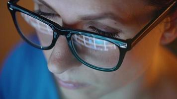 Woman in glasses looking on the monitor and surfing Internet at night. The monitor screen is reflected in the glasses video