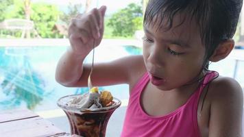 Wet little girl in a swimsuit eating ice cream by the outdoor pool during family summer vacation. Summer lifestyle concept. video