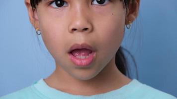 närbild av leende ung flicka avslöjande henne skön vit tänder på en blå bakgrund. begrepp av Bra hälsa i barndom. video