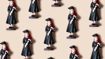 Pattern made from statuette in black graduate hat and gown on beige background. High quality footage video