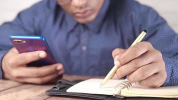 Man hand writing on notepad and using smart phone video