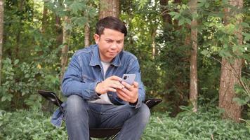 Asian man sitting with mobile phone under tree video