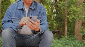 ásia homem sentado com Móvel telefone debaixo árvore video