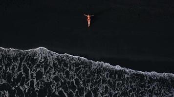 Haut vue de une fille dans une rouge maillot de bain mensonge sur une noir plage sur le le surf doubler. côte de le île de Ténérife, canari video