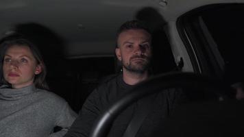 Couple riding in a car is upset because they are stopped by a police patrol at night. Flashing lights visible in the rear window. View inside car video