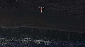 Haut vue de une fille dans une rouge maillot de bain mensonge sur une noir plage sur le le surf doubler. côte de le île de Ténérife, canari video