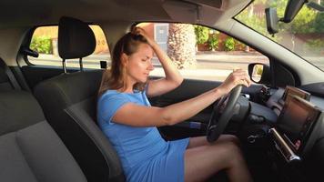 femme dans une bleu robe est assis dans le voiture, attache sa siège ceinture et met le clé dans le allumage avant conduite video