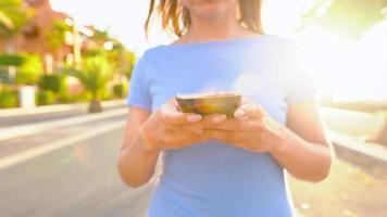 Woman in a blue dress using smartphone while walks on a palm street at sunset video