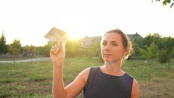 vrouw lanceert papier vliegtuig tegen zonsondergang achtergrond. concept van dromen over op reis of de beroep van een stewardess. video