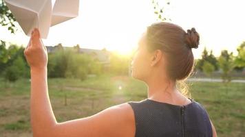 Woman launches paper airplane against sunset background. Concept of dreaming about traveling or the profession of a stewardess. video
